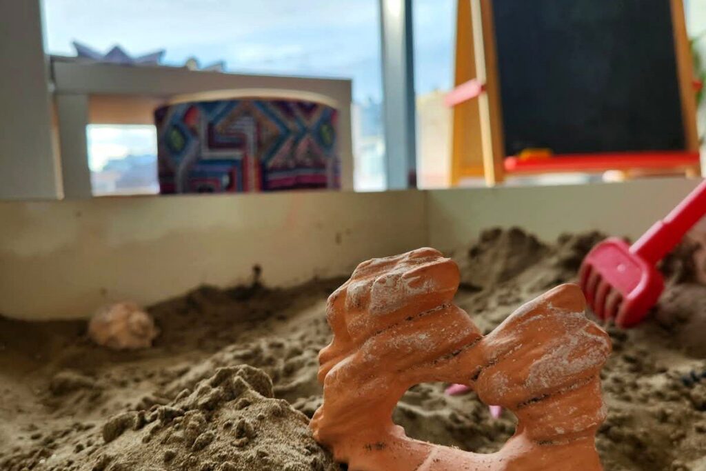 Oyun terapisinde kullanılan kum tepsisi ve minyatür figür, arkada kara tahta ve pencere